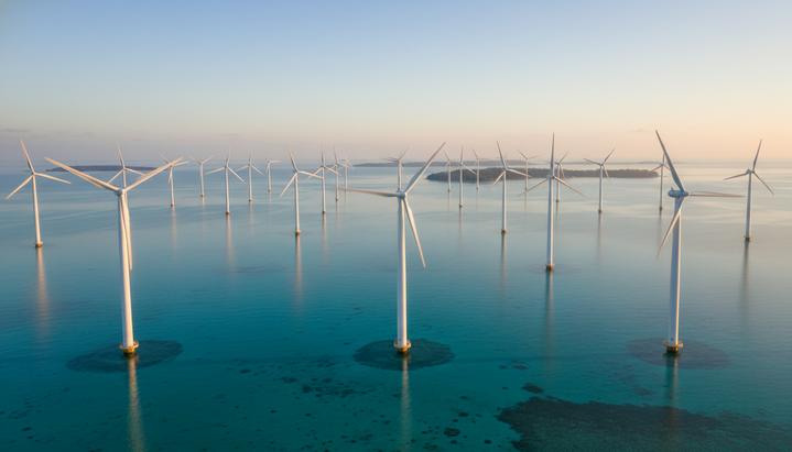 Морская ветроэлектростанция с рядами ветряных турбин в тропическом море на рассвете. На горизонте видны острова.