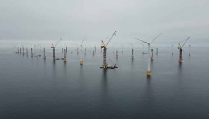 Морская ветроэлектростанция в процессе строительства в океане. Часть турбин установлена, рядом с недостроенными стоят краны.