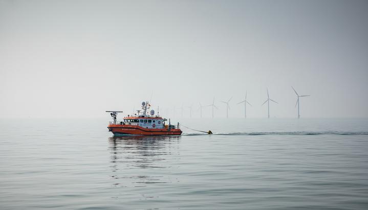 Fugro и PTSC G&S поддержат развитие морской ветроэнергетики Вьетнама Беспилотное исследовательское судно в море у побережья Вьетнама, на горизонте видны силуэты морских ветряных турбин.
